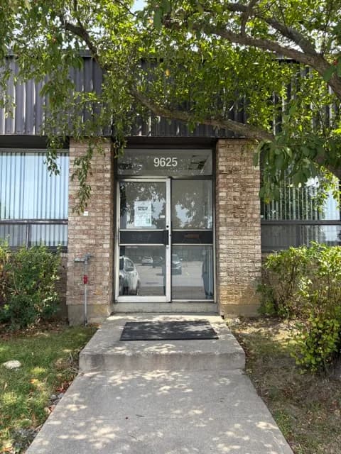 The Marché CTFO entrance seen from the parking lot: a glass door numbered 9625, set between two brick pillars under a tree.
